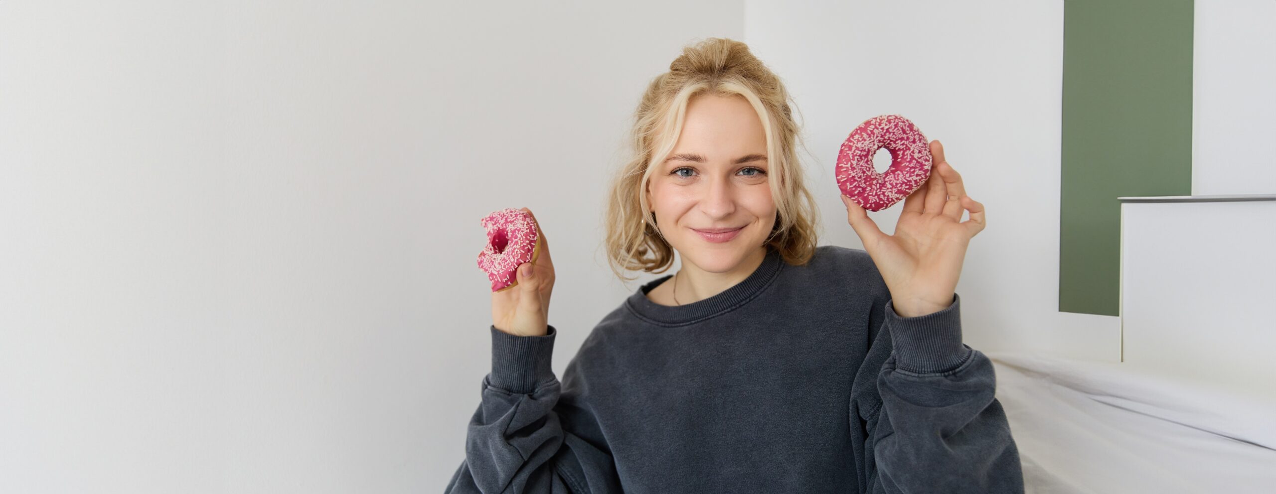 Close up portrait of happy, cute blond woman, holding doughnut, eating sweet, delicious comfort food, showing dessert at camera